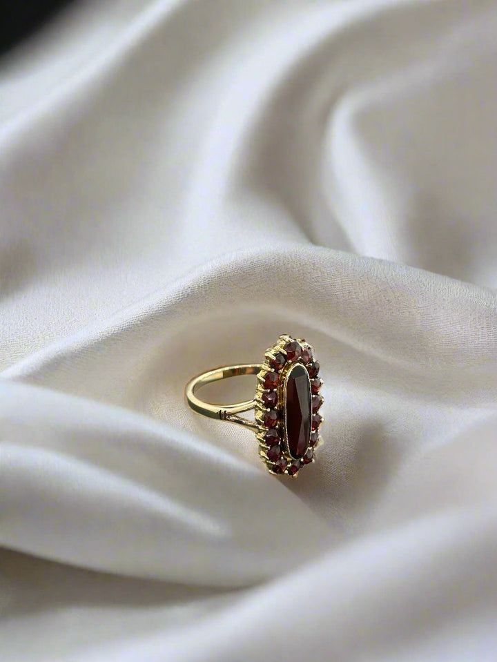 De vintage gouden ring 14k ovale granaat 3,7gr van Juwelier van der Kooij rust elegant op een witte, zijdeachtige stoffen achtergrond.