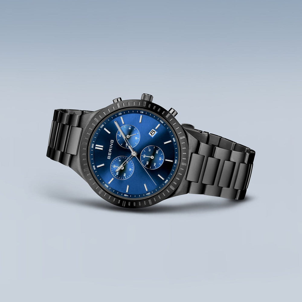 Het Bering-horloge 11743-727 is een stijlvol zwart polshorloge met een blauwe wijzerplaat met drie subwijzerplaten, een datumvenster, zilveren uurmarkeringen, een nauwkeurig Quartz-uurwerk en een metalen schakelband tegen een grijze achtergrond.