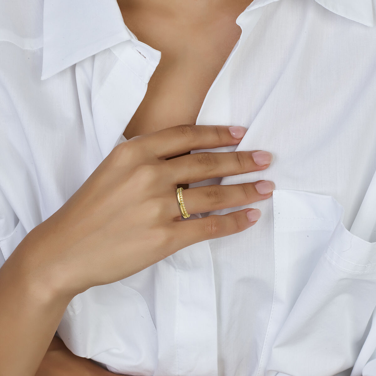 Een persoon in een wit overhemd met knoopsluiting raakt zachtjes zijn borst aan, waardoor de ringbolletjes 14K geelgoud van Van der Kooij Collectie worden benadrukt: een tijdloos damessieraad.