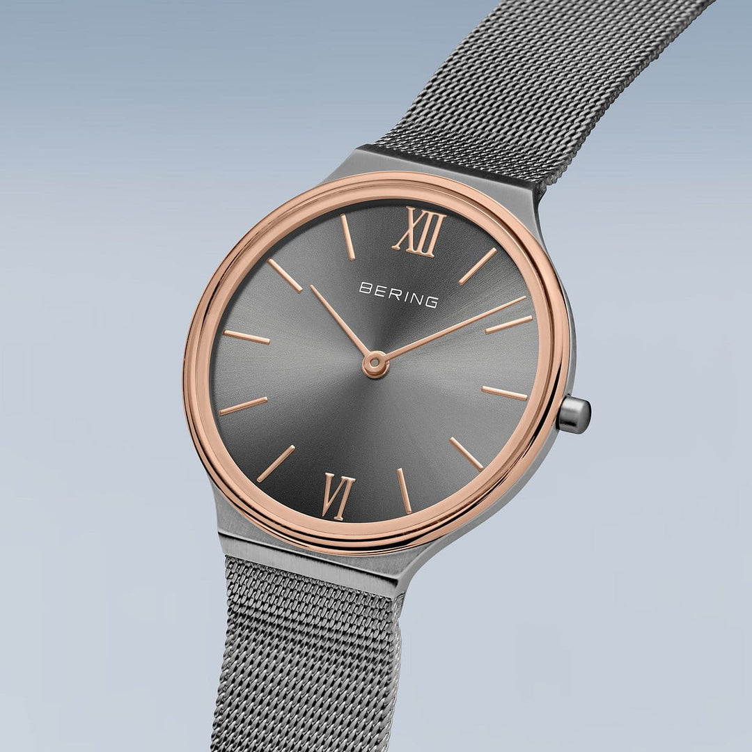 Het Bering dameshorloge grijze wijzerplaat - 18434-369 heeft een antracietgrijze wijzerplaat met een minimalistisch ontwerp en roségoudkleurige accenten, Romeinse cijfers op 12 en 6, eenvoudige uurmarkeringen, quartz uurwerk, een metalen mesh-band tegen een lichtblauw kleurverloop en duurzaam saffierglas.