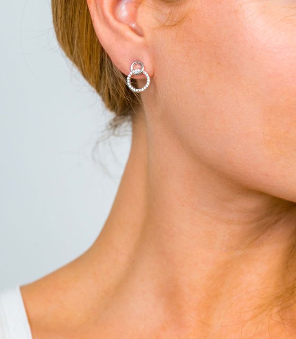 Close-up van het oor van een vrouw met Zinzi Oorbellen Zilver Zio1782: elegante zilveren oorbellen met een cirkelvormig ontwerp, kleine lus en ingebedde kristallen van Zinzi. Slechts een deel van haar gezicht en hals is zichtbaar tegen een lichte achtergrond.