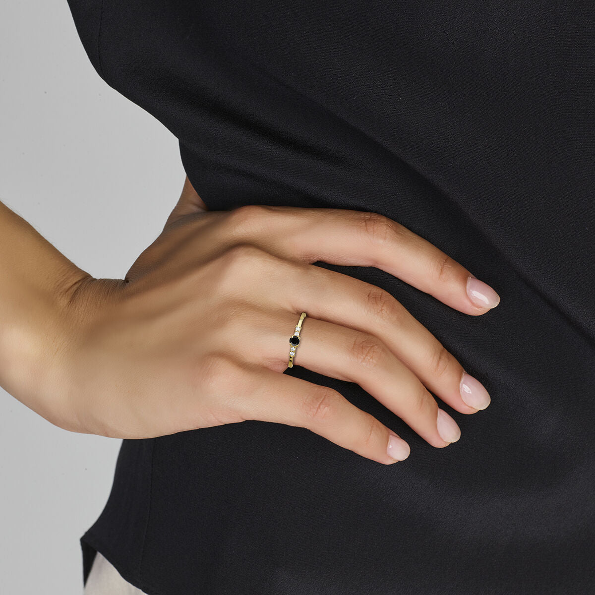 Een close-up van een verzorgde hand die de Van der Kooij Collectie ring zwart en wit zirkonia 14K geelgoud draagt, rustend op de heup tegen zwarte stof.