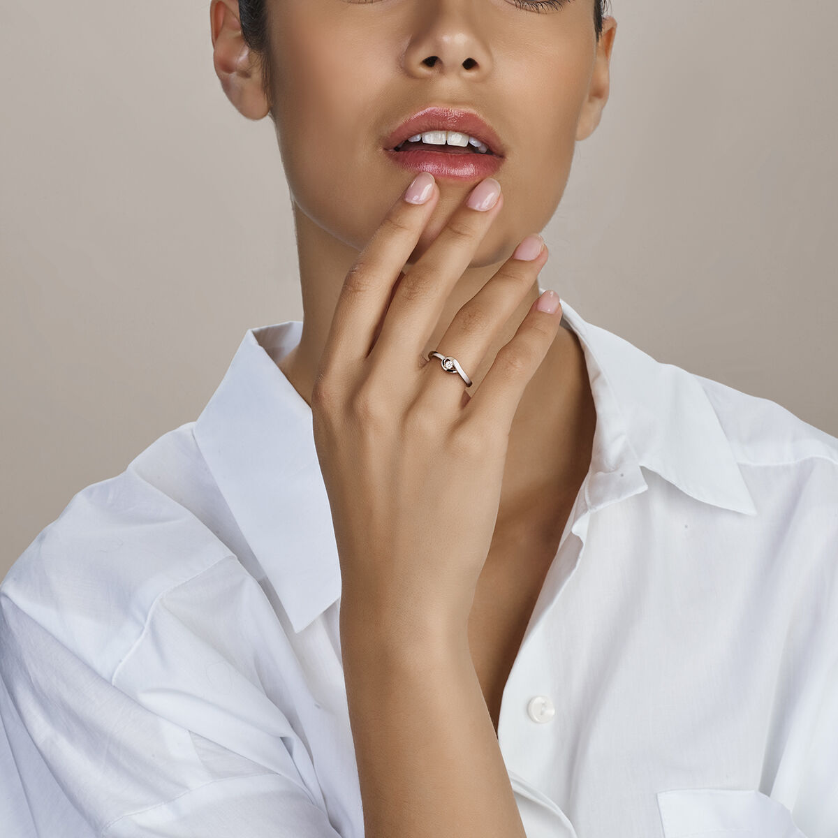 Een vrouw in een wit overhemd raakt zachtjes haar gezicht aan en benadrukt de Van der Kooij Collectie ring zirkonia poli/mat zilver gerhodineerd aan haar gemanicuurde vinger. Haar lippen zijn lichtjes gespleten.