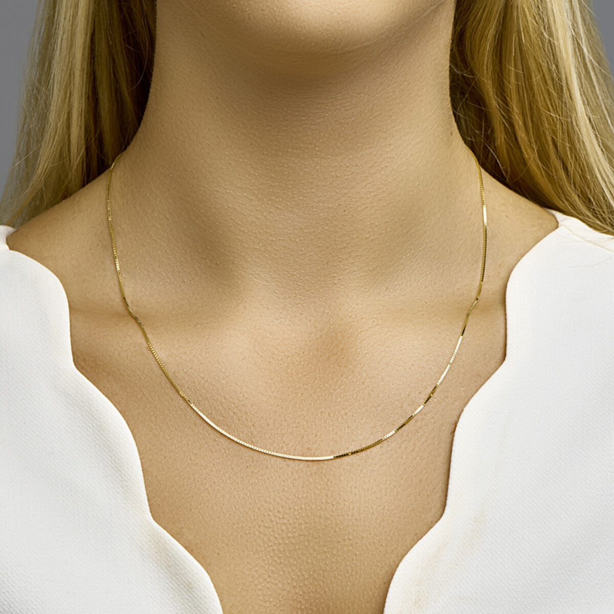 Een vrouw draagt het Van der Kooij Collectie collier venetiaans 0,8 mm 14K geelgoud met een witte top met V-hals. Alleen haar nek, ondergezicht en bovenborst zijn zichtbaar: een ideale look voor elke sieradencollectie.