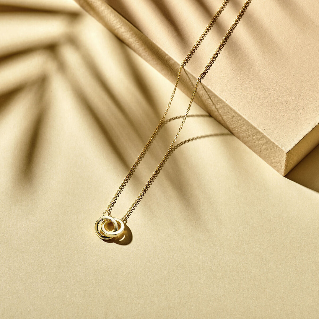 De Van der Kooij Collectie collier rondjes (40-42-44 cm) in 14K geelgoud schittert op een beige oppervlak met zachte schaduwen en geometrische vormen-het perfecte dames sieraad voor elke stijlvolle look.