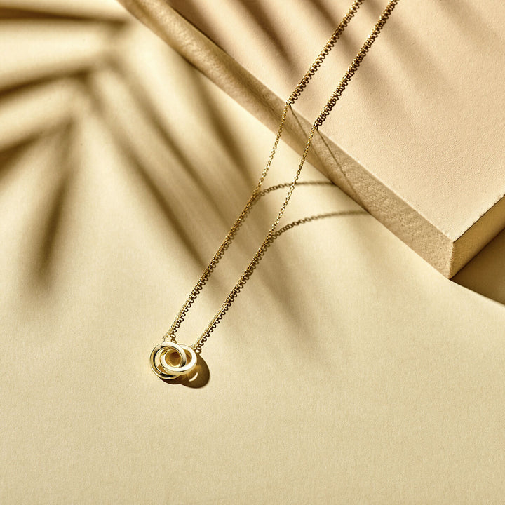 De Van der Kooij Collectie collier rondjes (40-42-44 cm) in 14K geelgoud schittert op een beige oppervlak met zachte schaduwen en geometrische vormen-het perfecte dames sieraad voor elke stijlvolle look.