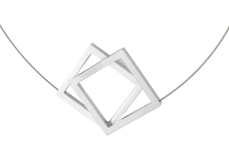 De Collier Twee grote vierkanten C104 van CLIC Creations is een minimalistische ketting met twee in elkaar grijpende open vierkante hangers in een zilveren afwerking. Handgemaakt in Nederland, het heeft een geometrisch ontwerp op een dunne draadketting, wat een moderne en stijlvolle look biedt tegen wit.