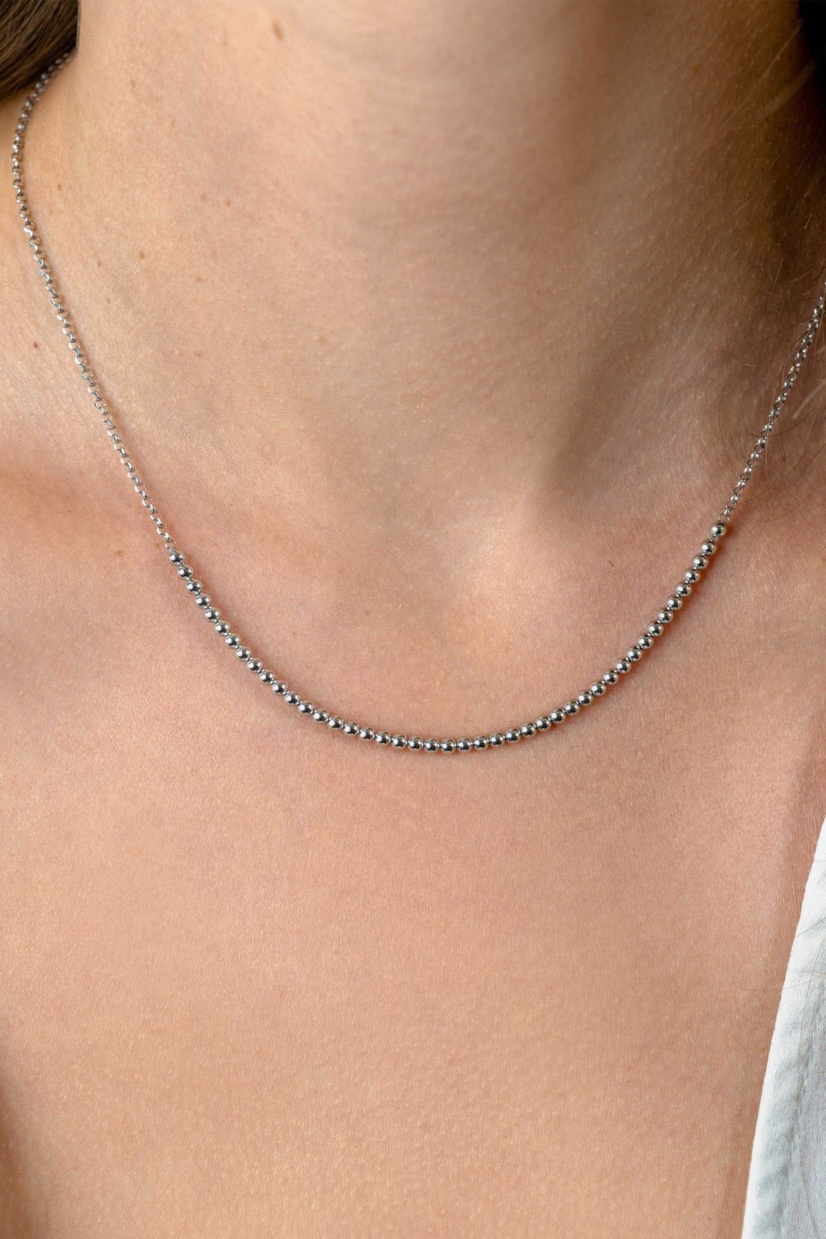 Een close-up van een hals die de Zinzi Ketting Zilver ZIC2640 van Zinzi draagt, met delicate zilveren kraaltjes, tegen een lichte huid. Rechtsonder is een wit topje zichtbaar.