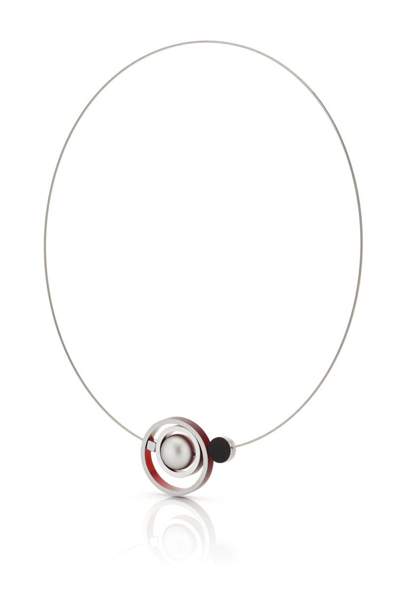 De Collier Ringen in elkaar Rood C187R van CLIC Creations is een minimalistische ketting met een dunne draad en een hanger met concentrische ringen in zilver, rood en zwart rond een parelachtige kraal. Handgemaakt in Nederland, het reflecteert prachtig licht tegen de effen witte achtergrond.