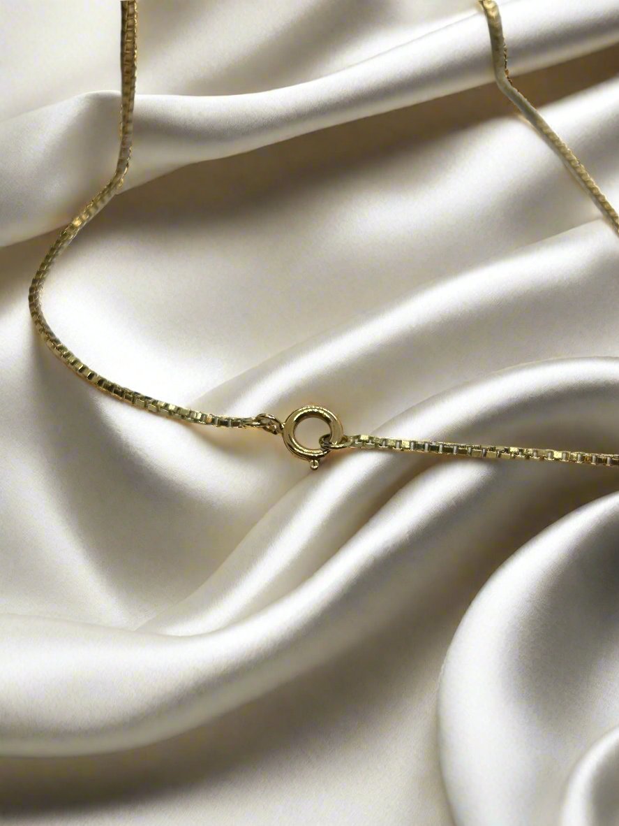 Het vintage gouden collier 60cm 18K Venetiaans, weegt 4,5 gram en is van Juwelier van der Kooij. Het heeft een ronde sluiting en rust elegant op ivoorkleurige satijnen stof, waardoor er zachte rimpelingen ontstaan.