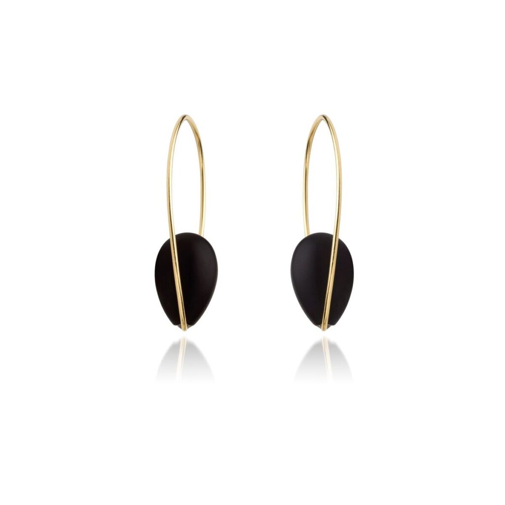 De Geelgouden oorbellen met onyx van Sanne Kickken zijn minimalistische gouden oorbellen met een lang, gebogen draadontwerp en zwarte druppelvormige elementen, symmetrisch weergegeven tegen een effen witte achtergrond.