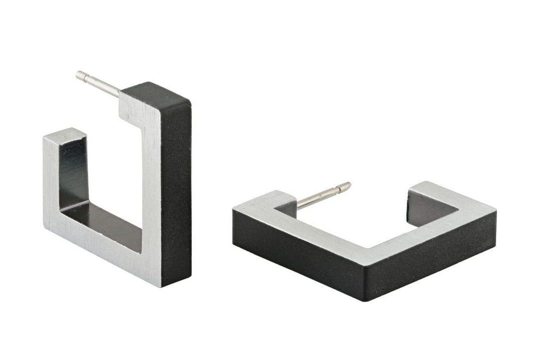 Er worden twee vierkante metalen oorbellen getoond, waarvan één geheel zilver en de andere met een zwarte voorkant. Beide zijn voorzien van hypoallergene, chirurgische roestvrijstalen pinnen voor comfort. Product: Vierkante creolen Zwart O11Z van CLIC Creations.