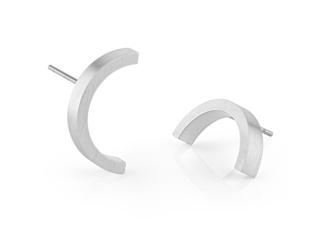 De Oorsteker Maan O48 oorbellen van CLIC Creations hebben twee halvemaanvormige stukken gemaakt van chirurgisch edelstaal met een matte afwerking op een witte achtergrond. De ene staat rechtop terwijl de andere sierlijk op het oppervlak kantelt.