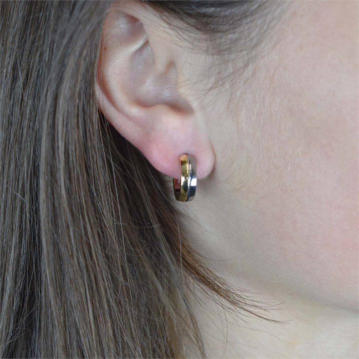 Close-up van het oor van een persoon met steil bruin haar, die een Boccia Titanium Oorring Bicolor 0539-07 draagt. De kleine, goud-zilveren oorbel van Boccia steekt af tegen de zacht wazige achtergrond en benadrukt het elegante ontwerp.