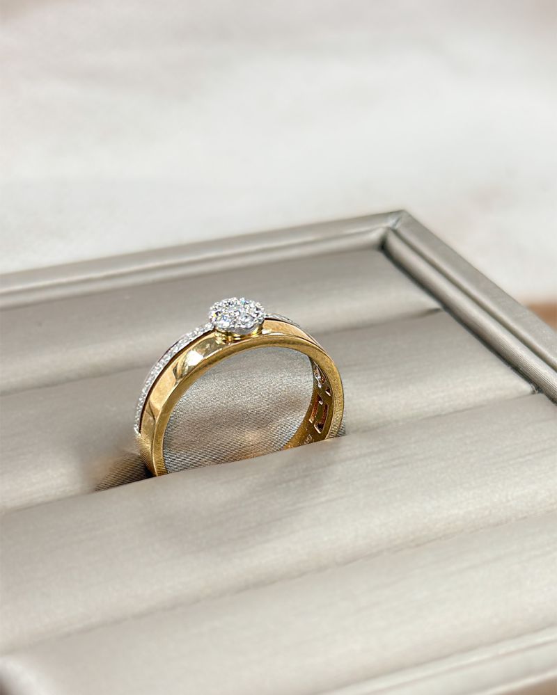 De Bicolor Wit- en Geelgouden Ring met Diamanten Roset - 0.22 crt van Excellent Jewelry heeft een ronde, met diamanten bezette zetting en wordt getoond op een lichtgrijze, gedempte juwelendoos.