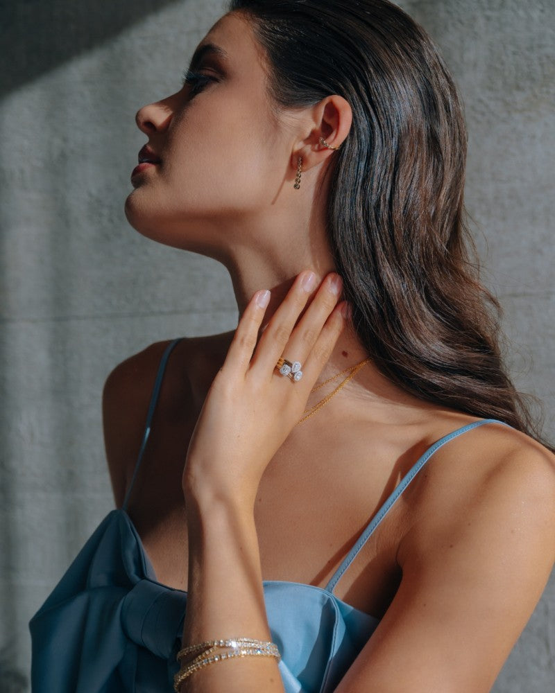 Een vrouw in een blauwe jurk toont elegant de 14k Bicolor Gouden Ring met Smaragdgeslepen Diamant in Entourage Zetting van Excellent Jewelry.