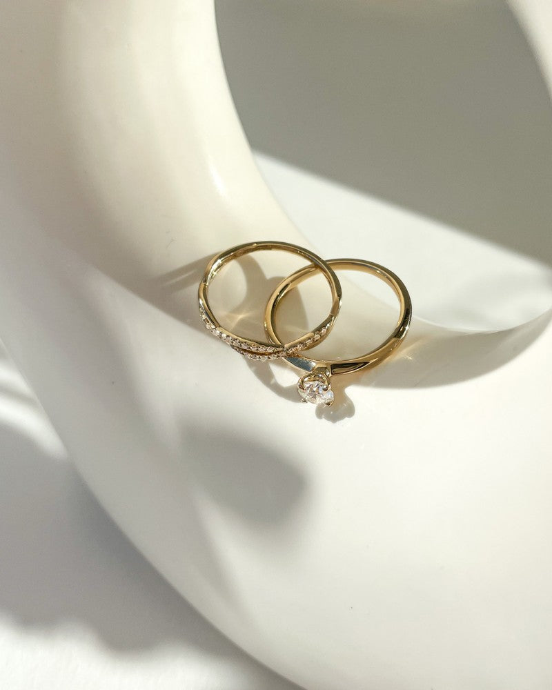 Twee gouden ringen van Excellent Jewelry rusten op een glad wit oppervlak; de ene is de "Elegante Gouden Solitair Ring met 0,40 crt Briljant - Subtiele Luxe voor Dames" en de andere heeft kleine diamanten langs de band.