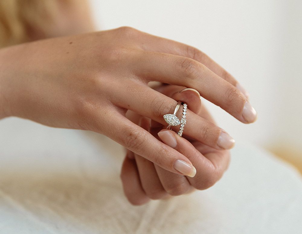 Een hand met gemanicuurde nagels draagt de Excellent Jewelry Witgouden Ring met Diamanten: Subtiele Elegantie in 14 Karaat, met een delicaat vlindermotief en fonkelende diamanten, tegen een zachte, neutrale achtergrond.